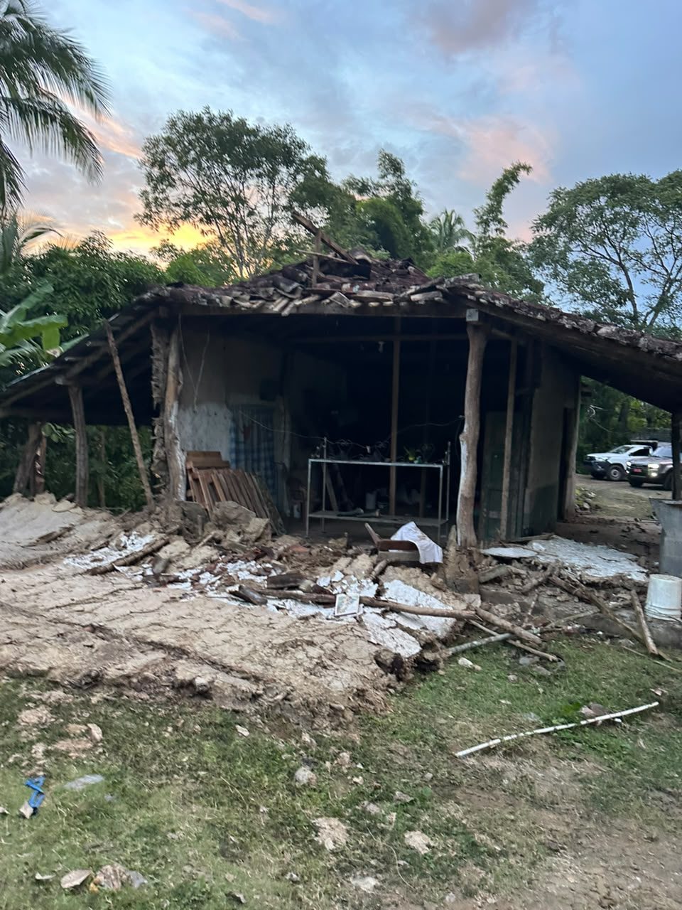 An old adobe house with a tiled roof, its front walls fallen into a heap of earth and timber.