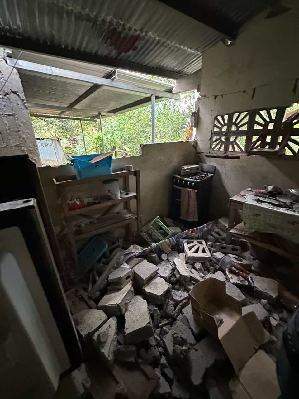 A kitchen where a wall has fallen in, with concrete blocks piled across the floor in front of a stove.