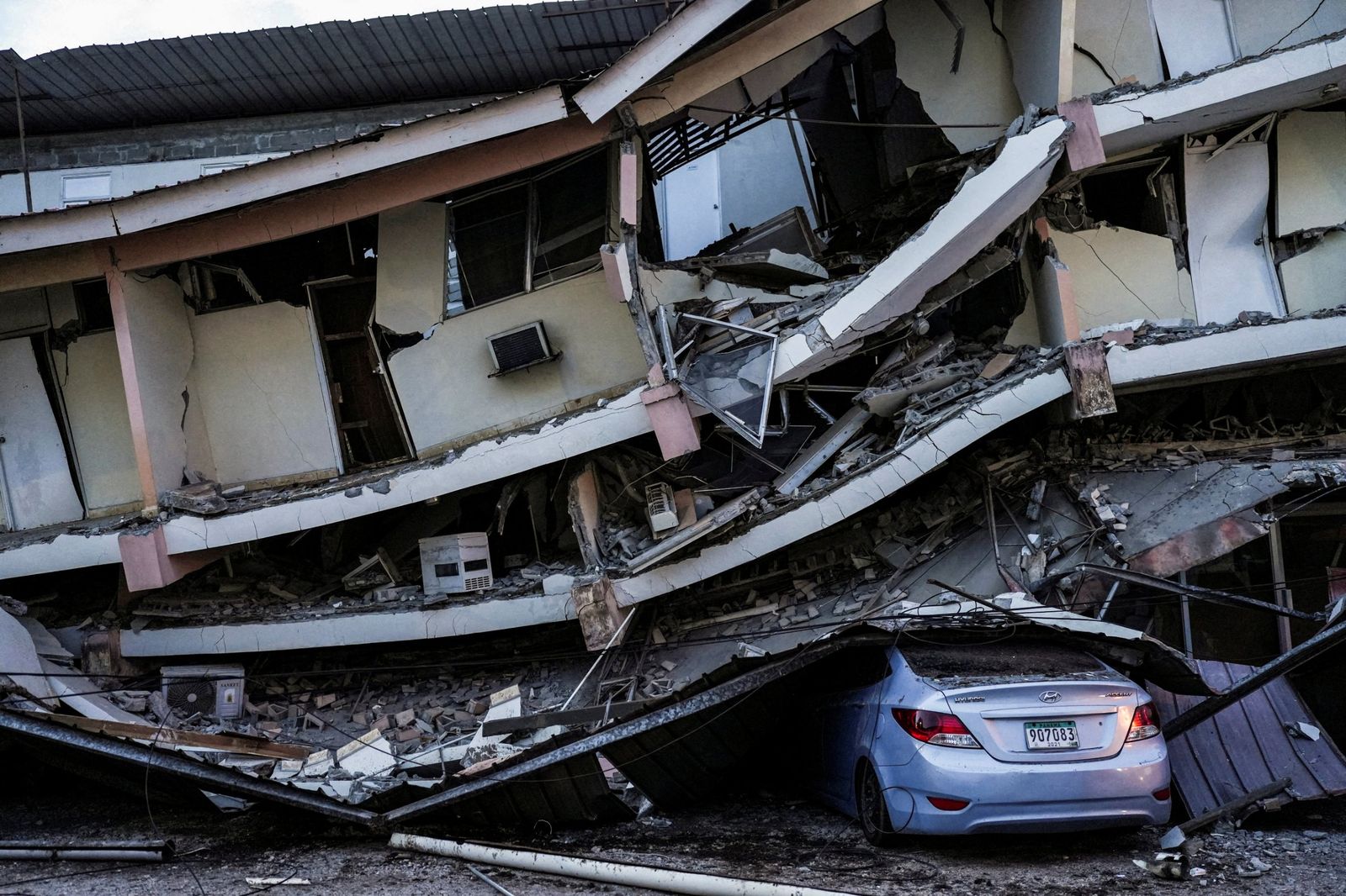 A multi-storey building collapsed onto itself, crushing a car parked underneath.