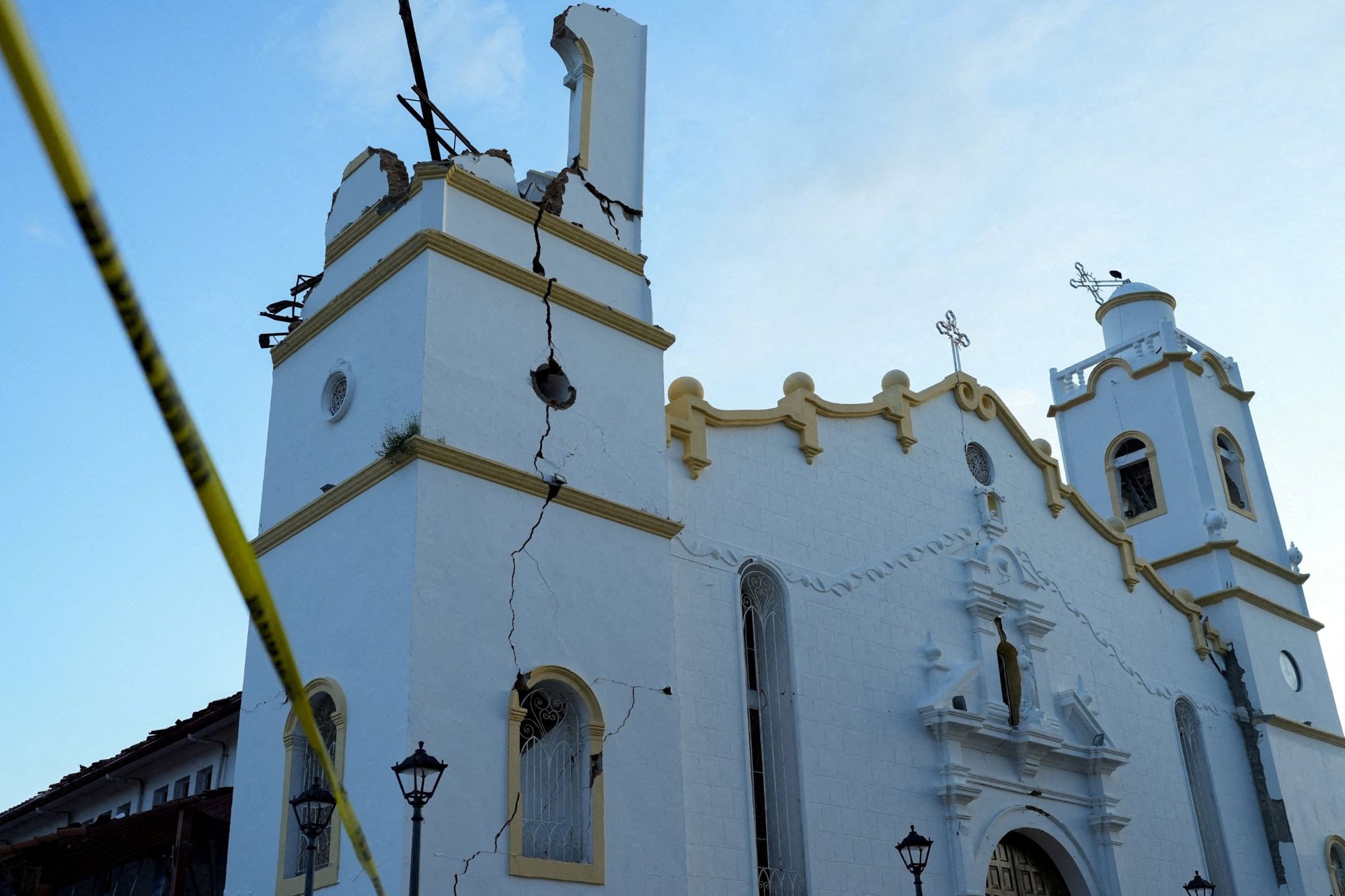 A white colonial church with a deep crack running down its bell tower, the top of which has collapsed.